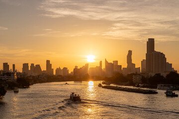 Golden sunrise over Chao Phraya River in Bangkok with boats and city skyline in the background of the Thai capital.