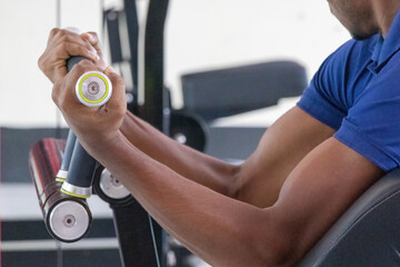 Close-up of a man's hand gripping a handle and lifting a plate-loaded bicep curl machine, showcasing focused muscle building and strength training in a modern gym.