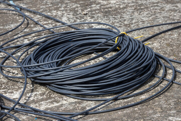 Close-up of a coil of black electrical wires, or cables, on a gray concrete floor, highlighting industrial, construction, and power themes.