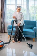 Senior Asian woman vacuuming living room while listening to music with headphones, looking at camera