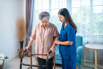 Elderly Asian woman walking with nurse assistance and walker at home