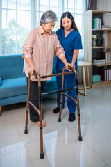 Senior elderly Asian woman using walker with caregiver support at home