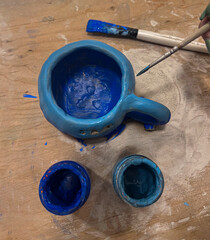 Handmade clay mug painted with blue acrylic paint on wooden table, symbolizing pottery craft,...