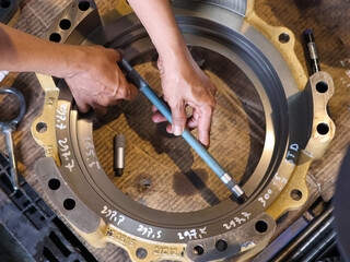 Close-up of a person's hands using a Tubular inside micrometer to measure a drum piston. The image focuses on the industrial process, highlighting precision, quality, and the technical tools involved.