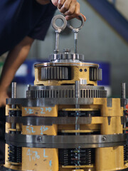 Worker handling planetary gear assembly with chain hoist, highlighting mechanical engineering and machinery maintenance process.