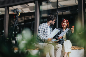 Two colleagues review and discuss documents while sitting in a vibrant outdoor area, emphasizing workplace collaboration and a casual professional environment.
