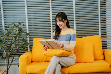 Happy young asian woman use headphones and relaxing at home.Female smile sitting on sofa,couch and holding mobile smartphone.Listening to music on lazy and radiating joy and relaxation.