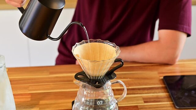 Msn pouring hot water into coffee dripper to make fresh filter coffee on wooden table