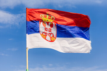 Waving national flag of Serbia fluttering against a bright blue sky on a sunny day, embodying pride...