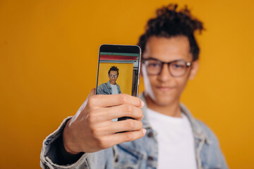 Making photo of himself by smartphone. Young guy is against yellow background