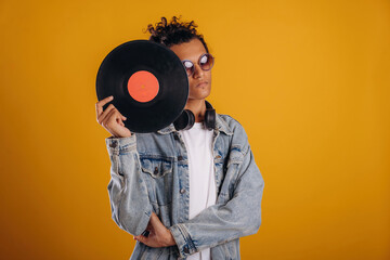 Fototapeta premium Conception of music, holding vinyl record, with headphones on neck. Young guy is against yellow background
