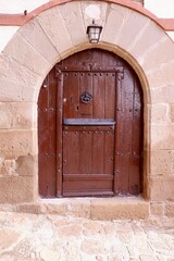 A sturdy wooden door with a handle and a mail slot is set in a rough stone archway.