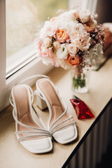 Bridal shoes with decorative crystals placed on a wooden floor, partially hidden under a wedding dress.
