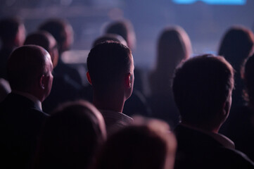 Rear view audience during Gdynia conference, spotlight head rim lighting, landscape telephoto bokeh, engaged mood, useful for corporate keynote brochure