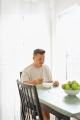 Adult Male Enjoying a Bowl of Granola Indoors with Natural Light.