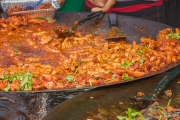 A large pan of spicy chicken curry is being cooked and served at Brick Lane Market in London, UK