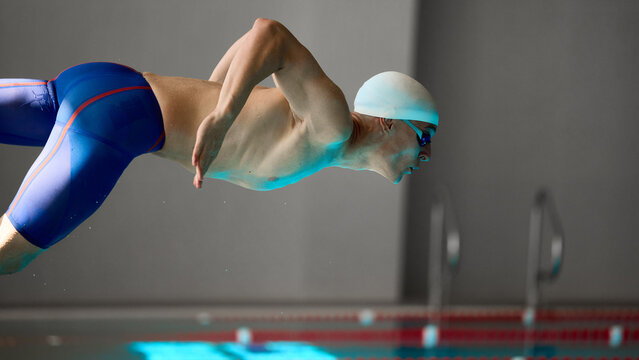 Male swimmer in close-up streamlined dive motion during professional start. Concept of motivational posters, fitness wellness, sports advertising, swimming education, and medical context.