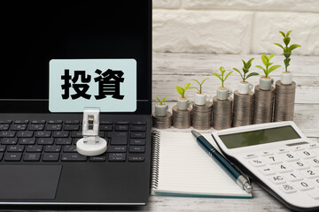 ノートパソコンと積みあがったコインと電卓で投資のイメージ