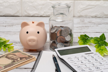 電卓と豚の貯金箱と硬貨とノートで家計のイメージ