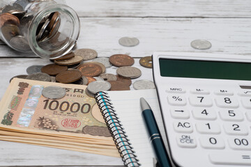 電卓と一万円札と瓶からこぼれた小銭でお金のイメージ