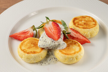 Four delicious cheesecakes on a white plate are garnished with poppy seed sauce and fresh strawberries