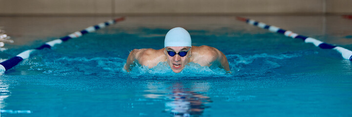 Male swimmer performing butterfly stroke with intensity. Concept of competitive sport, motivation, fitness content, rehabilitation, and swimming technique education with strong emotion. Banner