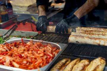 Skilled chef in black gloves grilling meat on a barbecue, surrounded by vibrant fresh ingredients, showcasing culinary expertise and the art of food preparation in a lively outdoor setting