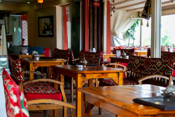 Cozy restaurant interior featuring wooden tables and intricately designed chairs, adorned with vibrant textiles, creating a warm and inviting atmosphere for dining and social gatherings