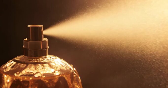 Pressing decorative glass perfume bottle nozzle releasing fine golden mist in studio, copy space