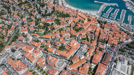 aerial view of area around old town in Menton, France, with historic buildings, French Riviera coastline with "Plage des Sablettes" and parts of port "Vieux Port de Menton" in background