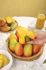 Fresh Hainan Guifei Sweetheart Mangoes in Wicker Basket with Tropical Fruit Juice on White Table