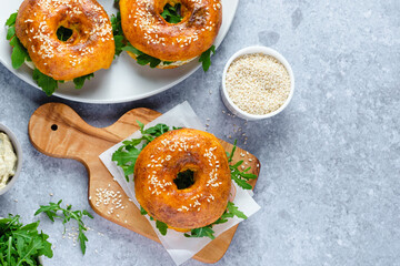Three freshly baked bagels filled with greens and ham, on a wooden board and plates. Bagel breakfast sandwiches a zesty unique twist. top view