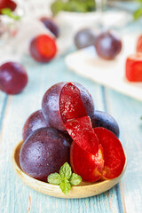 Fresh Red Plums in Wooden Bowl with Mint Garnish on Rustic Blue Wood Background