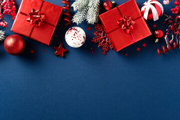 Red Christmas gifts and festive decor with baubles, stars, and pine branches on dark blue background. Holiday flat lay with copy space