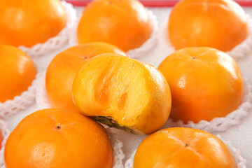 Fresh Ripe Persimmons in Protective Packaging with Cut Open Fruit Showing Orange Flesh