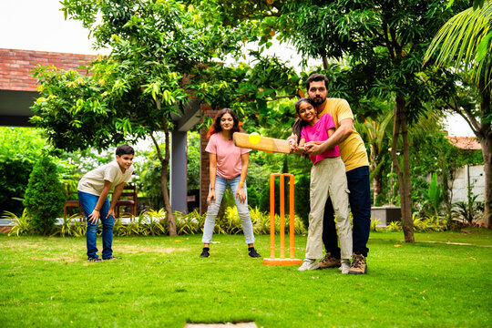 Indian Asian family bonding through outdoor cricket batting in garden, enjoying fun and play