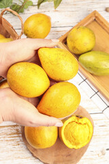 Fresh Golden Hainan Mangoes in Hands with Wooden Crate on Rustic White Background