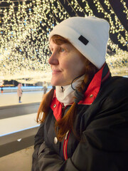 Woman in white hat enjoying winter skating rink with festive holiday lights