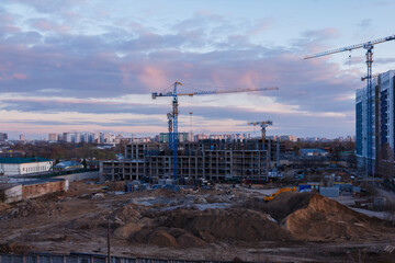 Urban construction site with cranes and heavy machinery at sunset in city