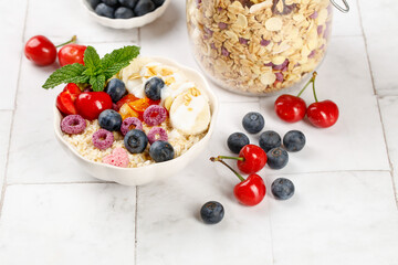 Healthy Oatmeal Breakfast Bowl with Fresh Berries Yogurt and Granola on White Wood Background