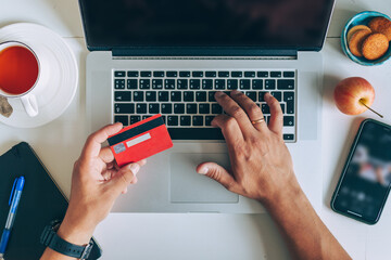 Man using laptop and holding credit card on desk with coffee cup and notebook. Concept of online...