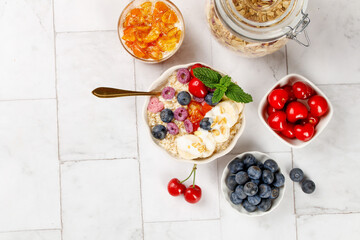 Healthy Oatmeal Breakfast Bowl with Fresh Berries Yogurt and Fruit on White Marble Background