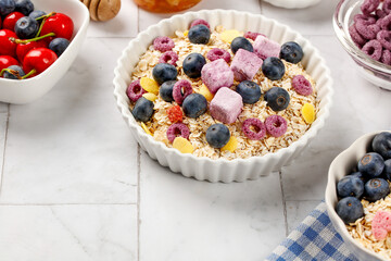 Nutritious oatmeal breakfast bowl with berries, fruit chunks and yogurt treats on rustic white wood background