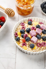 Healthy Oatmeal Breakfast Bowl with Fresh Berries and Yogurt Chunks on White Wood Background
