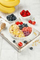 Healthy Breakfast Bowl with Oats Fresh Berries Cherries and Banana on Rustic White Wooden Tray