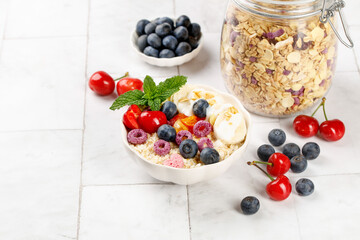Healthy Oat Breakfast Bowl with Yogurt Berries and Granola Jar on White Wood Background