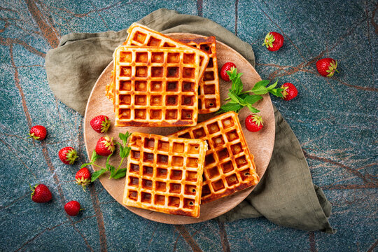 Fresh baked homemade Brussels waffles with fresh strawberries served as top view on a wooden plate