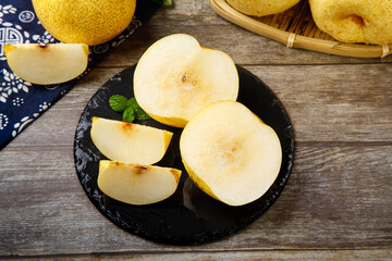 Fresh Asian Pears Sliced on Black Plate with Bamboo Basket on Wooden Background