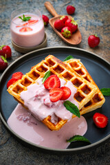 Fresh baked homemade Belgian Brussels waffles with yogurt fresh cream cheese topping dessert and fresh strawberries served as close-up in a design plate