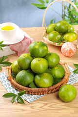 Fresh Green Citrus Fruits in Wicker Basket on Wooden Table with Tea Cup and Natural Kitchen Decor